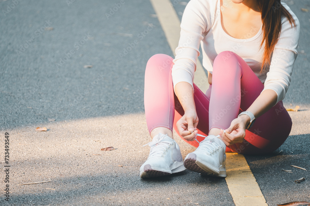 Fitness concept, Close-up of a woman sitting on the pavement, tying her white running shoes, ready for a workout in nature.