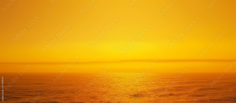 A hazy image of the sun setting over the ocean, casting a warm amber glow across the fluid water. The sky is filled with vibrant red and orange clouds, creating a stunning natural landscape.