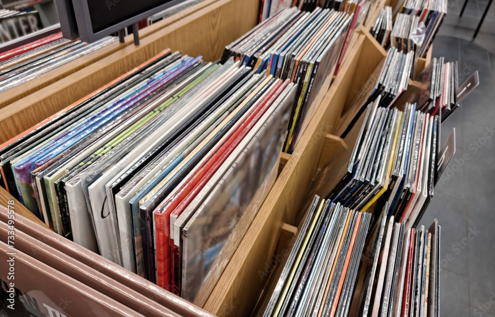 Obraz premium Large collection of vinyl records displayed in wooden bins, diverse popular music album selection at a music store, shop, supermarket. Musical albums pressed on vinyl, fresh releases, buying selling
