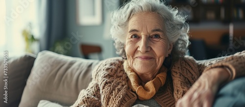 An elderly woman with wrinkles is sitting on a couch, gesture of joy as she smiles happily at the camera, sharing a moment of fun at the event photo
