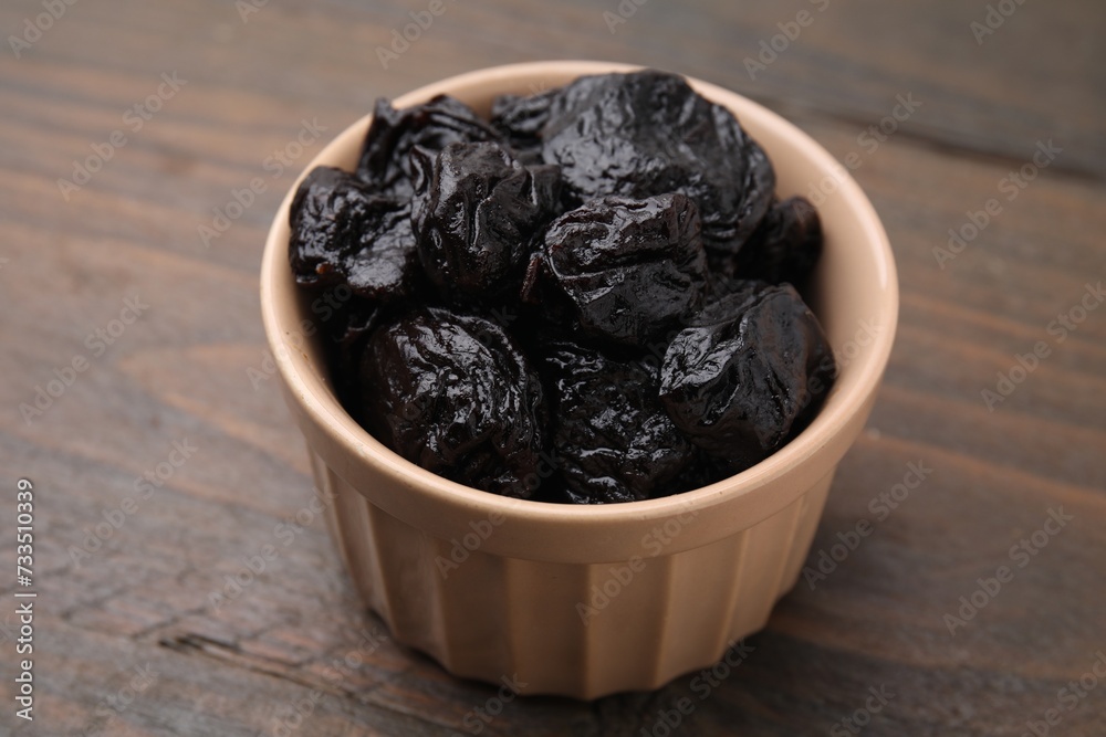 Sweet dried prunes in bowl on wooden table, closeup
