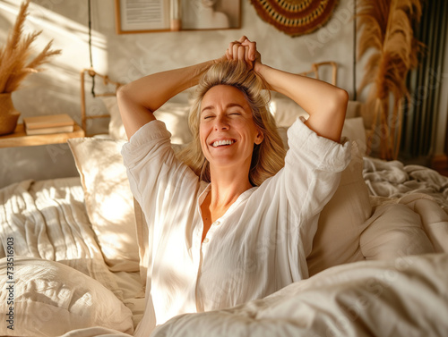 A content middle-aged woman wakes up happily, stretching in bed and enjoying the peacefulness of waking up naturally. In her cozy bedroom, an older lady sits up with a radiant smile after a restful sl