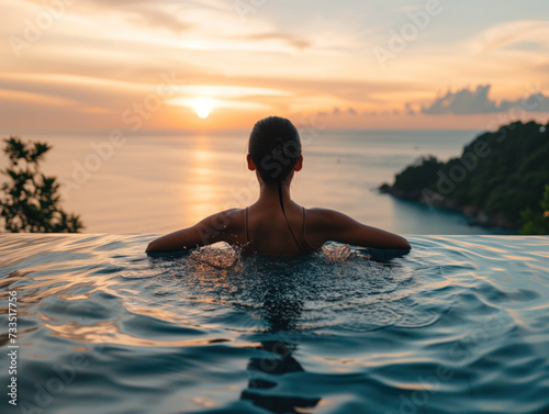 An Asian woman enjoys her summer retreat, gracefully splashing water in an infinity pool with a majestic sunset view of the blue sea. She is embracing in tranquility and bliss