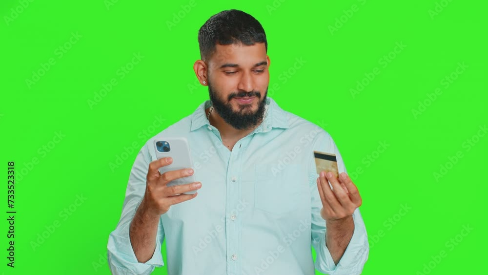 Happy young Indian man using credit bank card and smartphone while transferring spending money, purchases online shopping, ordering food delivery. Arabian guy isolated on green chroma key background Happy young Indian man using credit bank card and smartphone while transferring spending money, purchases online shopping, ordering food delivery. Arabian guy isolated on green chroma key background
