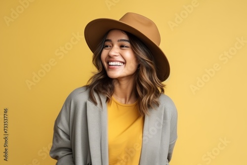 Portrait of a beautiful young woman with hat laughing over yellow background