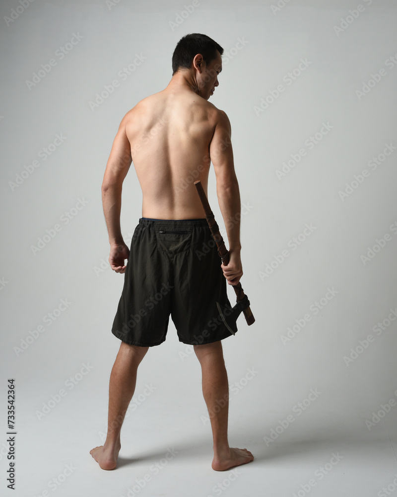 Full length portrait of fit handsome shirtless asian male model,  Holding viking axe weapon, standing in warrior training action pose, isolated on white studio background.