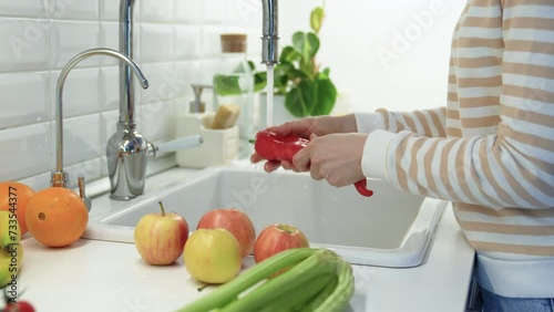 Washing of red ramiro pepper under tap water. Oranges, apples, celery lying on table. Healthy tasty raw sweet fresh fruit and vegetables full of vitamins, used for salad cooking. Natural nutrition photo