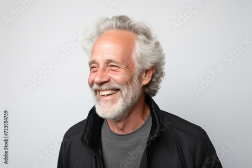 Portrait of a happy senior man smiling at the camera on grey background © Iigo