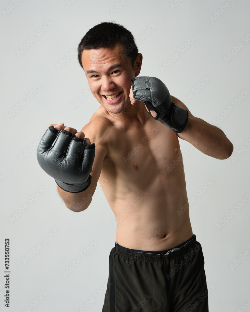Close up portrait of fit asian male model, shirtless with muscles. Wearing gym shorthand boxing gloves, gestural punching pose. Isolated on a white studio background. Close up portrait of fit asian male model, shirtless with muscles. Wearing gym shorthand boxing gloves, gestural punching pose. Isolated on a white studio background.