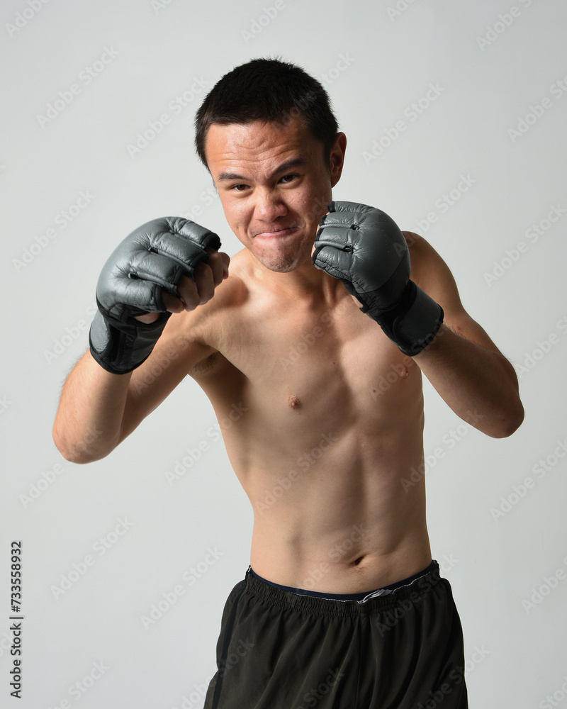 Close up portrait of fit  asian male model, shirtless with muscles. Wearing gym shorthand boxing gloves, gestural punching pose. Isolated on a white studio background.