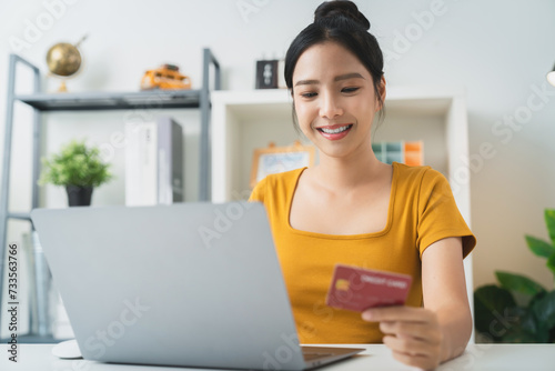 Young Asian woman holding credit card and using laptop for shopping online with payment on internet banking.