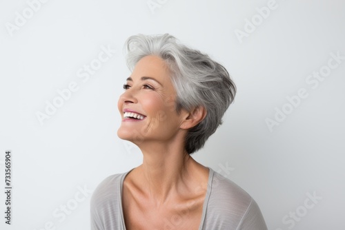 Portrait of happy senior woman looking up and smiling against grey background