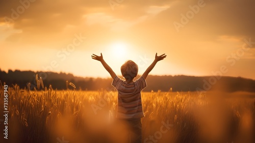 A little boy raises his hands above the sunset sky, enjoying life and nature. Happy kid on a summer field looking at the sun. Silhouette of a male child in the sun. Fresh air, environment concept. photo