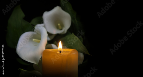 Candle flame and white calla lily in surrounding darkness