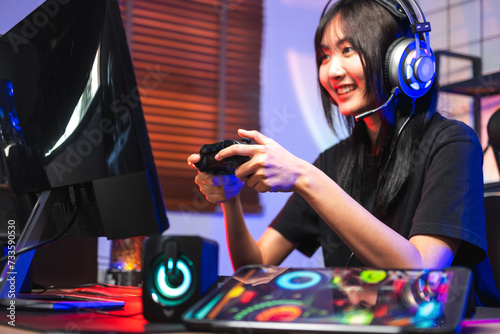 Happy asia girl gamer wear headphone competition play video game online with computer colorful neon light in living room at night