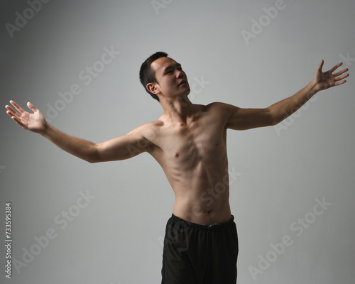 Close up portrait of fit asian male model, shirtless with muscles. gestural ti chi inspired posing with arms reaching out. Isolated on a white studio background with moody silhouette.