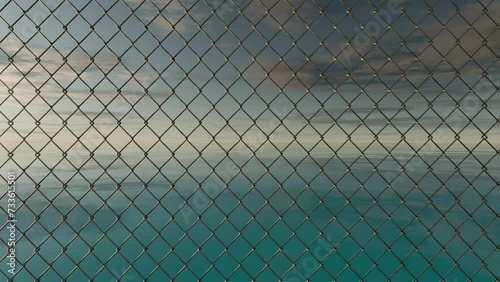 3D-rendered chain link fence with the background of a vast emerald ocean and sky in the time of sunset