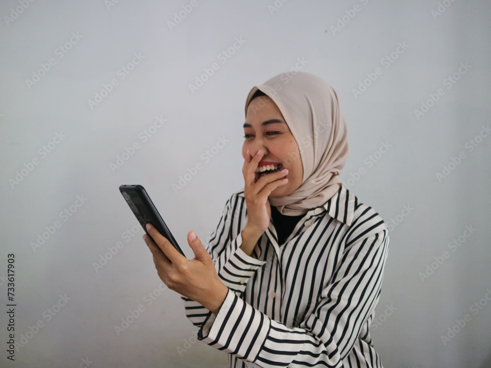Happy muslim woman reading very good and funny news on smartphone. Sporty woman with excited expression holding mobile phone. Hand in mouth. Happy muslim woman reading very good and funny news on smartphone. Sporty woman with excited expression holding mobile phone. Hand in mouth.