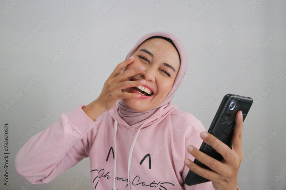 Happy muslim woman reading very good and funny news on smartphone. Sporty woman with excited expression holding mobile phone. Hand in mouth. Happy muslim woman reading very good and funny news on smartphone. Sporty woman with excited expression holding mobile phone. Hand in mouth.