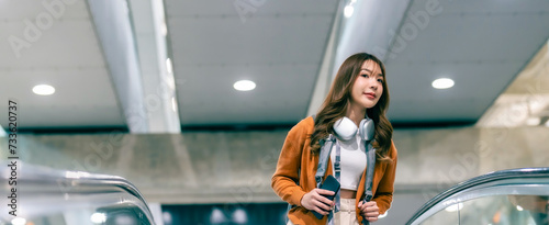 Young asian woman in international airport terminal or modern train station. Backpacker passenger female commuter walking on escalator