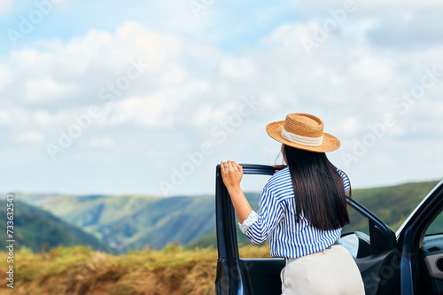 Back view of young beautiful woman traveling by car in the mountains, summer vacation and adventure