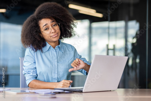Konstfotografi Upset black woman in blue shirt and eyewear making dislike gesture while working by desktop in office