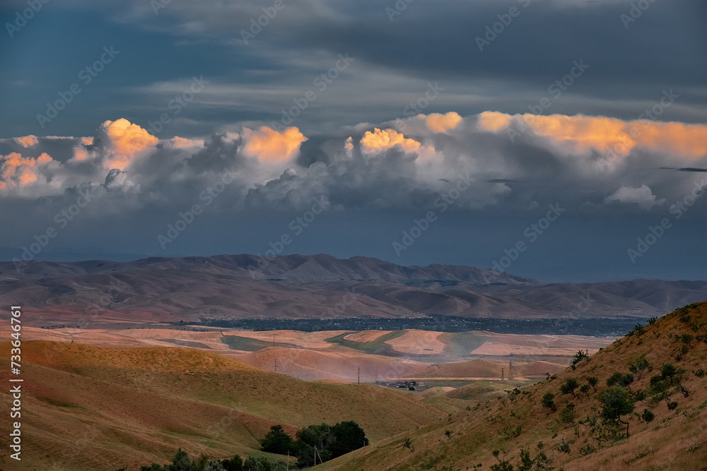 A beautiful, tranquil landscape with mountains against the backdrop of epic clouds illuminated by the setting sun.