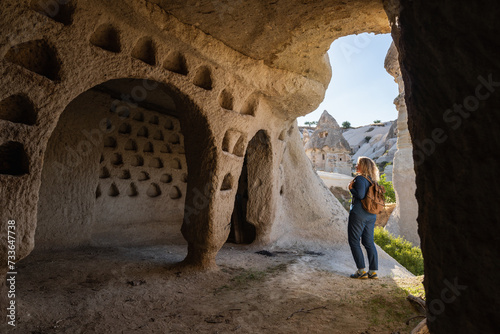 Woman traveling in Cappadocia, standing inside the cave with the view of the pigeon valley in Turkey