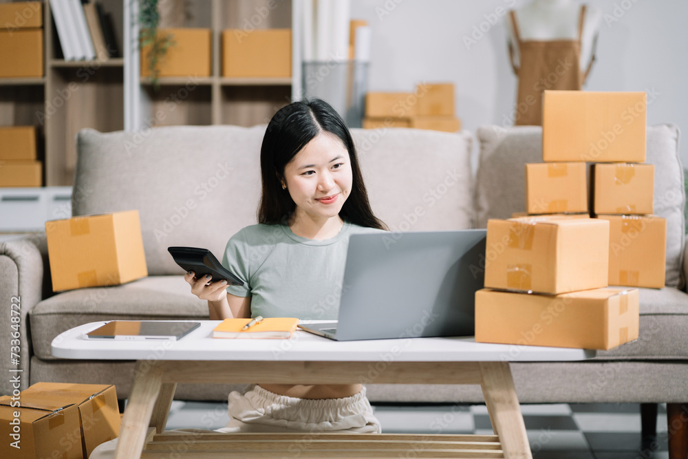 Entrepreneur using calculator in her hand, calculating financial expense at home office, online market packing box delivery,Startup successful small business owner, SME, concept. Entrepreneur using calculator in her hand, calculating financial expense at home office, online market packing box delivery,Startup successful small business owner, SME, concept.