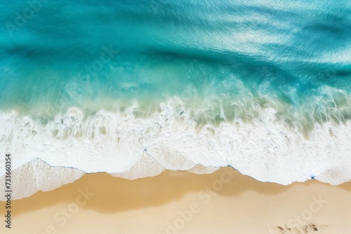 Aerial shot of turquoise waves crashing onto a sandy beach shore.