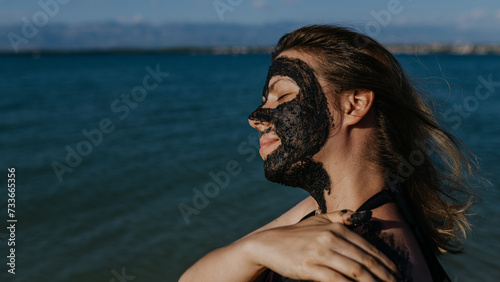 Woman applies healing mud to her face and body. Natural healing mud in Croatia on the beach. photo