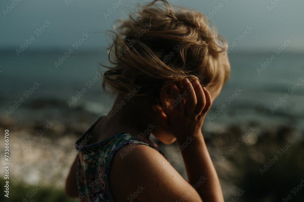 Side view of small girl with blonde hair standing at beach looking at sea. Side view of small girl with blonde hair standing at beach looking at sea.