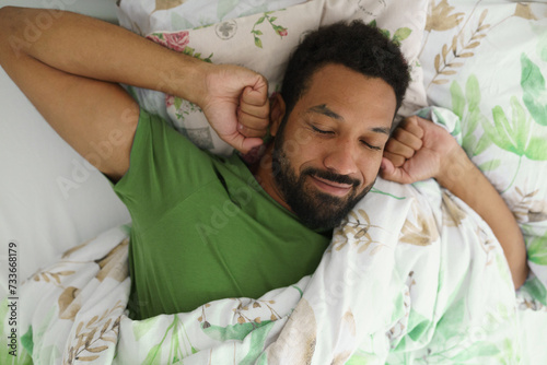 Top view of man waking up in bed, stretching arms, smiling in the morning. photo