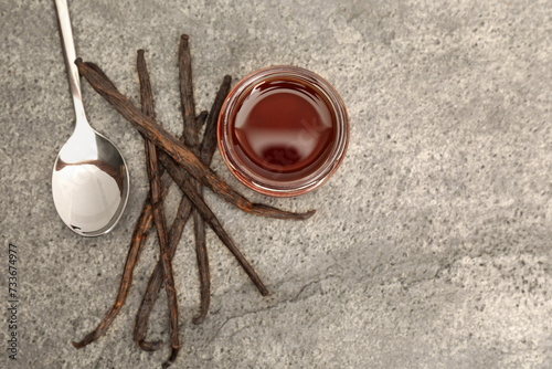 Aromatic vanilla extract and pods on grey table, flat lay. Space for text