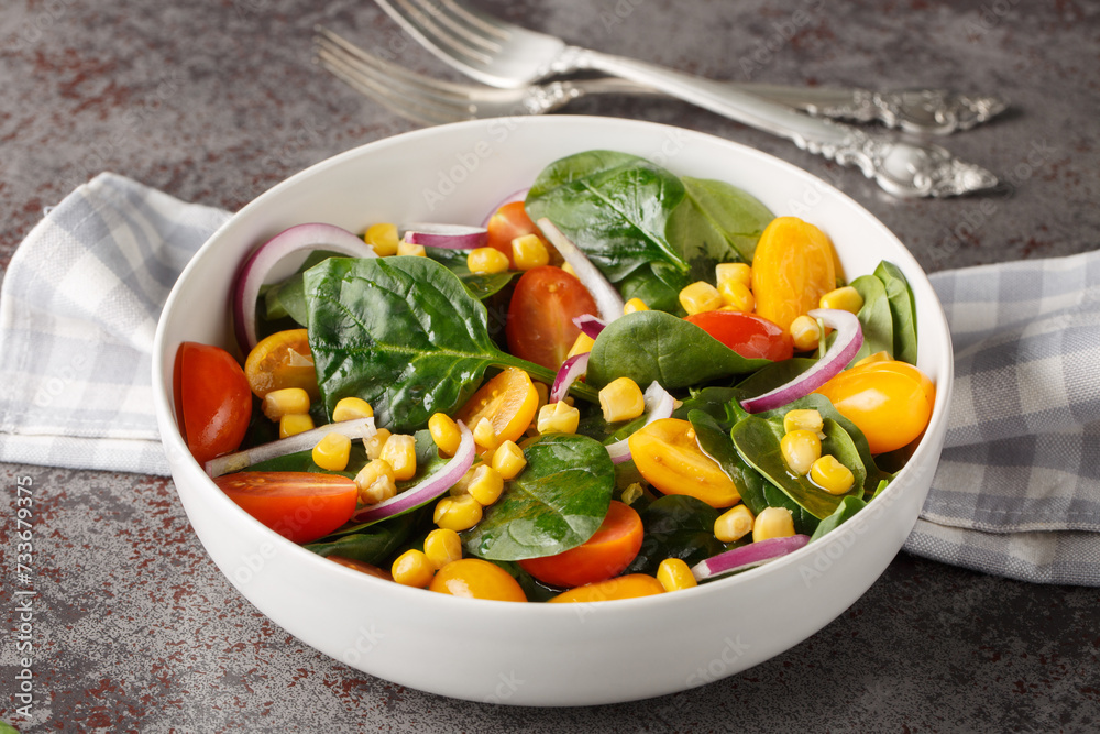 Light simple salad of fresh spinach, corn, cherry tomatoes and red onions with olive oil dressing close up in a bowl on the table. Horizontal