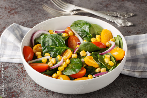 Light simple salad of fresh spinach, corn, cherry tomatoes and red onions with olive oil dressing close up in a bowl on the table. Horizontal