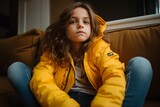 Portrait of a young girl in a yellow jacket sitting on a sofa.