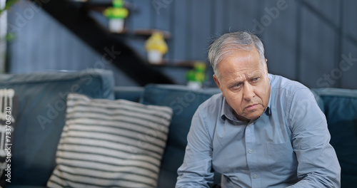 Worried retired Asian old senior man sitting alone sofa couch feel bad sorrow anxiety at indoor home. Indian elder aged Gray haired gen x male sad lonely pensive suffer ill health issues problem photo