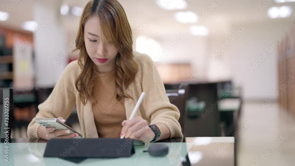 Young woman concentrating on writing with a stylus on a digital tablet in a library setting. Young woman concentrating on writing with a stylus on a digital tablet in a library setting.