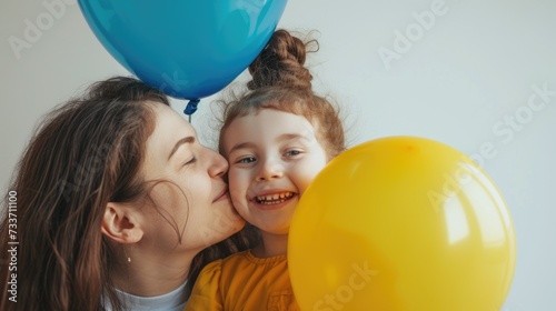 Portrait of happy mother and daughter hugging with two blue and yellow balloons, colors symbol of World Down Syndrome Day. White background. Autism, disability, solidarity, awareness