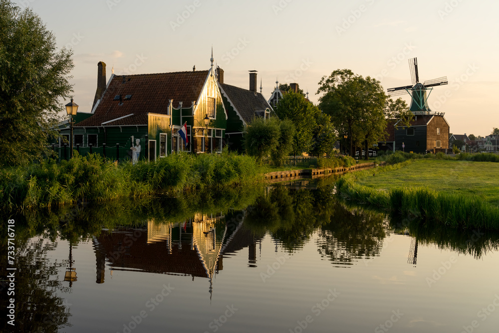 Beautiful village of Zaanse Schans in Netherlands at sunset with the wooden houses reflected on the canal in a sunny day. Netherlands. Beautiful village of Zaanse Schans in Netherlands at sunset with the wooden houses reflected on the canal in a sunny day. Netherlands.