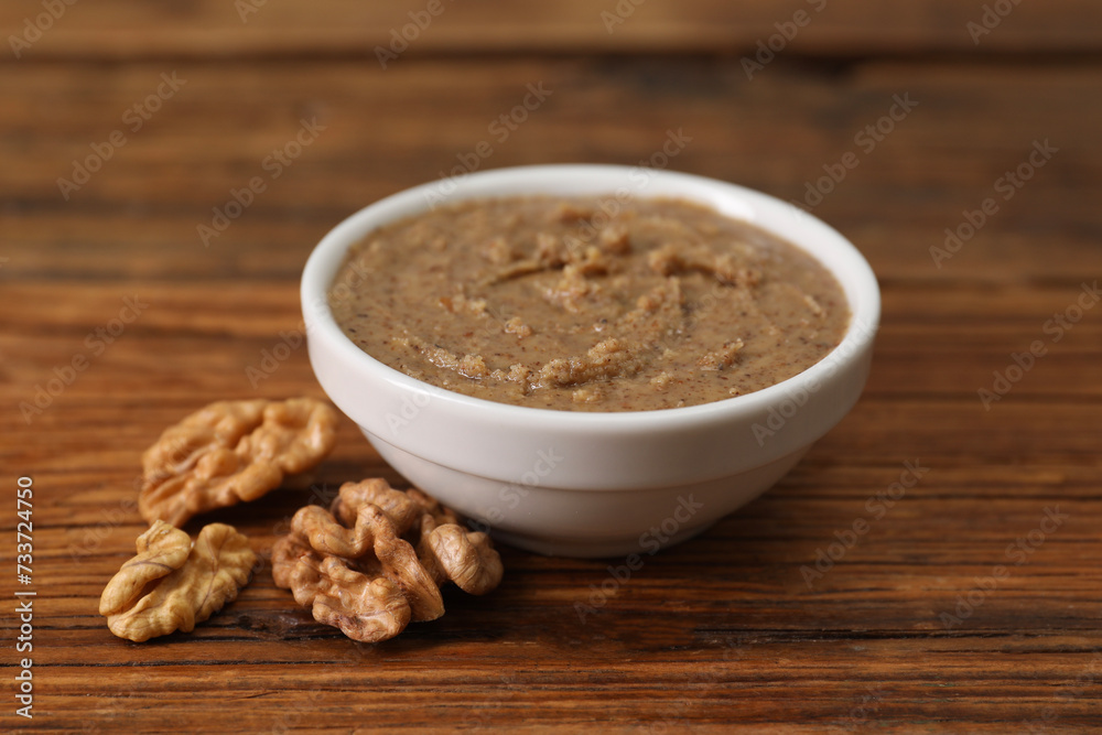 Delicious nut butter in bowl and walnuts on wooden table, closeup Delicious nut butter in bowl and walnuts on wooden table, closeup