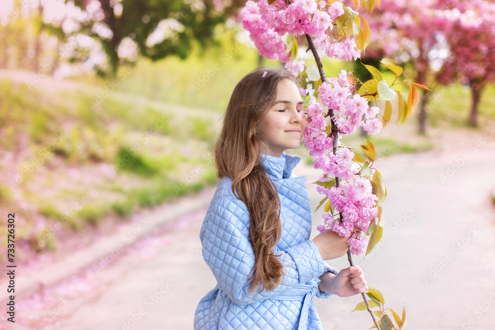 Young smile girl standing in dress at blossoming tree in the sakura garden. Beauty of woman and nature concept. Portrait of beautiful Little girl in white dress walking in blossom spring park. Young smile girl standing in dress at blossoming tree in the sakura garden. Beauty of woman and nature concept. Portrait of beautiful Little girl in white dress walking in blossom spring park.