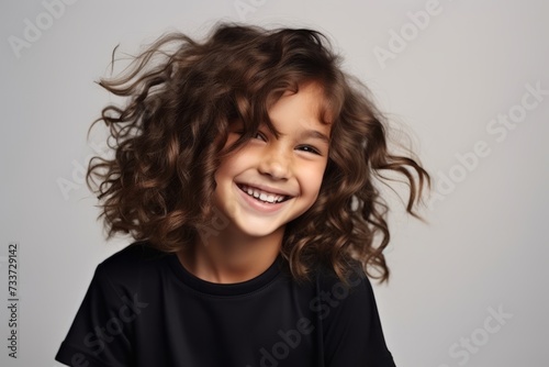 Portrait of a happy little girl with curly hair over gray background
