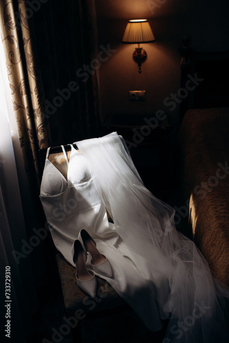 A modern wedding dress lies on a stylish chair in the soft morning light. Stylish wedding dress with sparkles shimmering in the light.