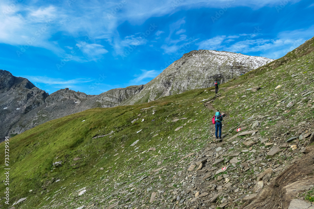 Two hikers with panoramic view of majestic mountain peaks of High Tauern, Carinthia Salzburg, Austria. Idyllic hiking trail in Goldberg group in wilderness of Austrian Alps. Wanderlust. Tranquil