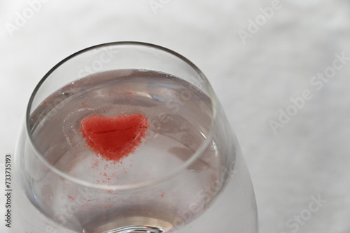 A pink ice cube is melting into the clear liquid in the glass