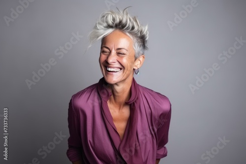 Portrait of a happy mature woman laughing against a grey background.