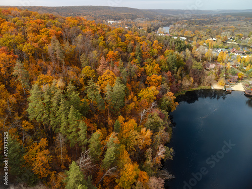 Autumn aerial river valley with colorful forest. Flying above autumnal vibrant trees near rural riverside in Ukraine