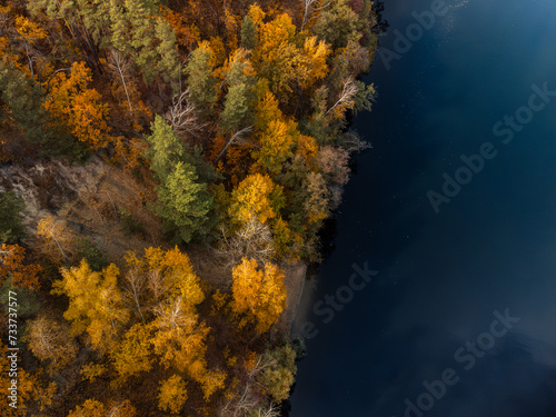 Autumn aerial drone look down view on river with colorful golden trees on riverbanks. Autumnal vibrant riverside